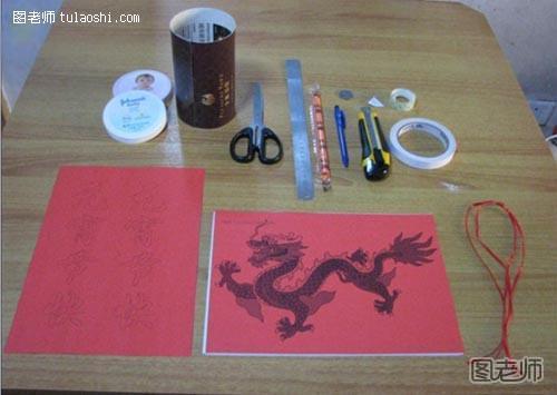 步骤1:准备材料：带图案的硬纸（或挂历纸）2张（A4）、硬纸1张（A4）、婴儿扑粉盒盖2个、剪刀、刻度尺、吸管、笔 、壁纸刀、透明胶布、双面胶、细红绳、一元硬币1枚。