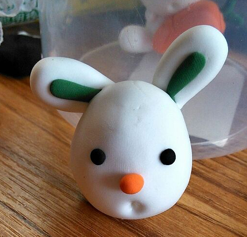 步骤5:搓两个黑色小圆，压扁，作眼睛，搓橘黄色小圆作鼻子，再用圆头棒按压出一个兔子的嘴巴