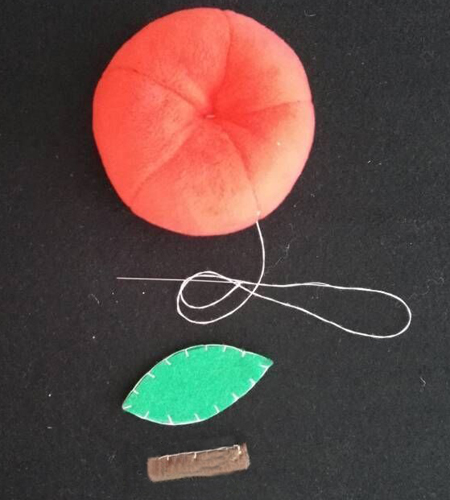 步骤4:填完BB棉缝合返口，用一根长针，从圆球的两头中间处穿线拉紧，依次反复几次固定出苹果形状。绿色叶子两片缝合，棕色柄卷起缝合，效果如图：
