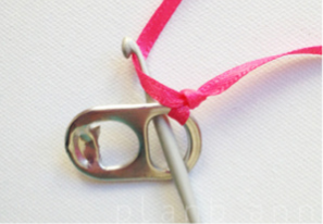 步骤2:将一根丝带在一个拉环上系一个单结，用钩针穿过拉环后面，勾住丝带长的一端